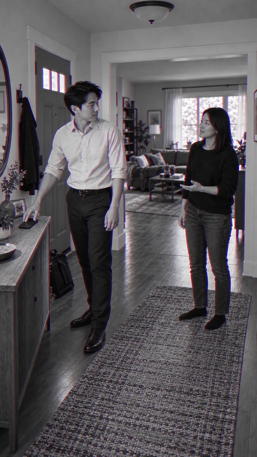 A man sets his phone down on the hall table as he comes in from work, his wife walking to meet him.