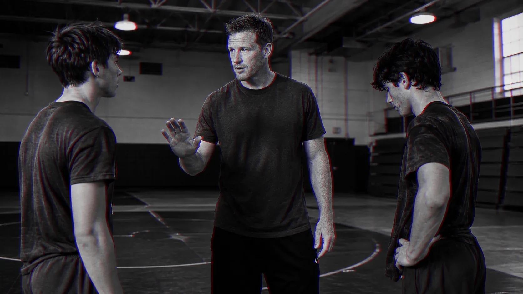 A coach steps between two young wrestlers on the mat, one hand raised, and sets the boundary.